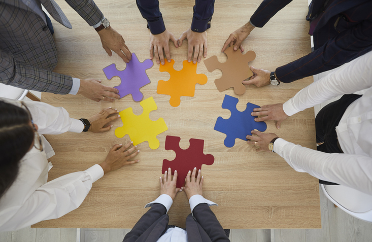 Top view of employees or workers brainstorm connect jigsaw puzzles involved in teambuilding activity in office. Diverse businesspeople team join pieces solve business solution. Teamwork concept.
